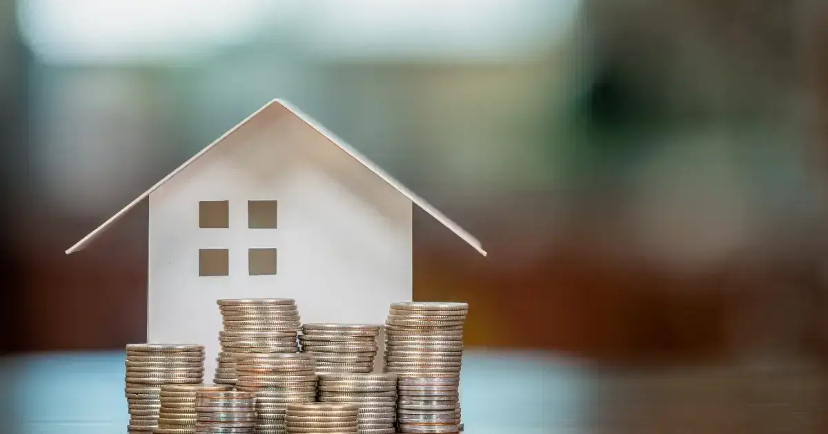 Small model of a home in need of a roof replacement with coins stacked in front of it
