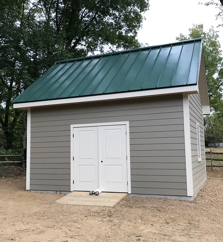 A detached shed with a green standing seam metal roof. 