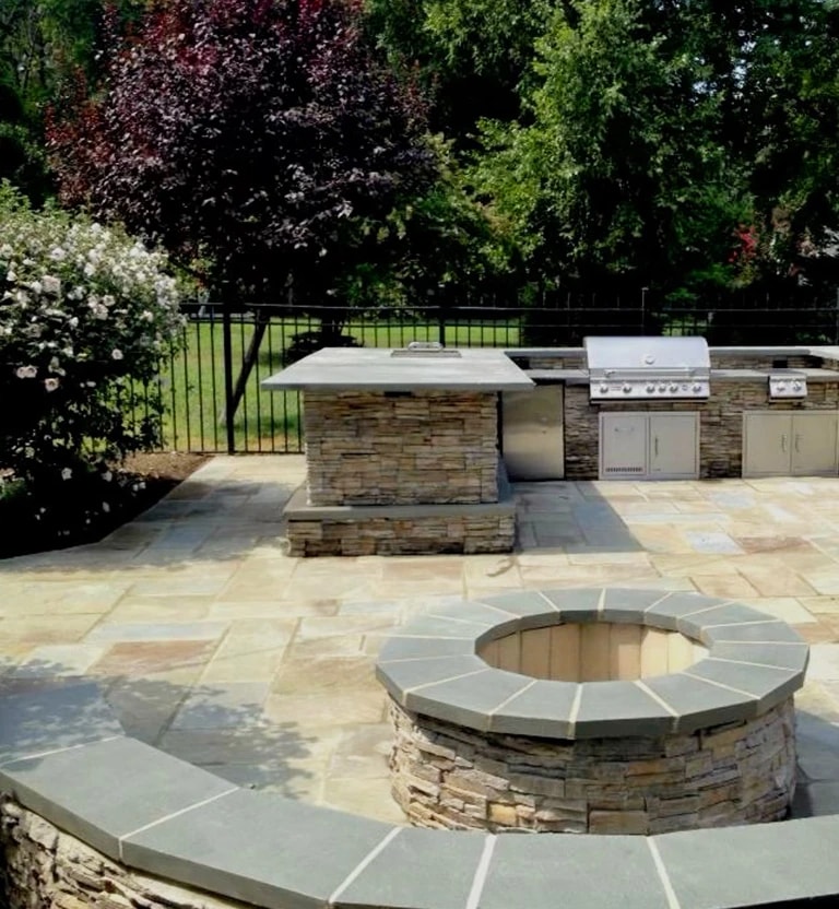 A stone outdoor living space with patio pavers and a stone firepit. 